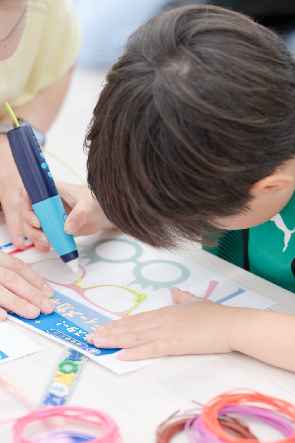 子どもが3Dペンで、ステンシルの上に線を描いている様子